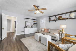 Living area featuring ceiling fan, dark wood-type flooring, and a textured ceiling