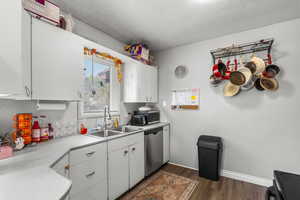 Kitchen with light countertops, dark wood-style flooring, white cabinets, stainless steel appliances, and a textured ceiling