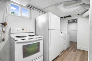 Kitchen with electric range, washing machine and dryer, light wood-type flooring, white cabinets, and light countertops
