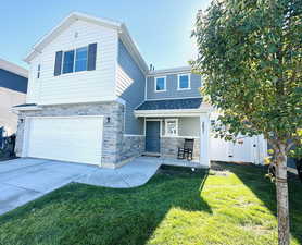 View of front facade featuring a front yard, stone siding, concrete driveway, and an attached garage