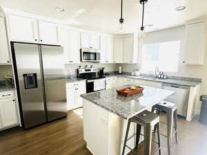 Kitchen with stainless steel appliances, light stone counters, a breakfast bar, dark wood-style floors, and a textured ceiling