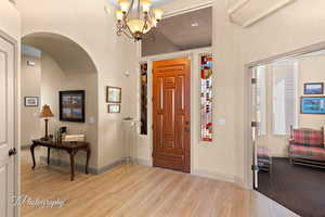 Foyer featuring arched walkways, light wood-style floors, and a chandelier