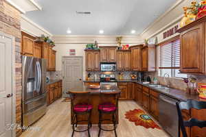 Kitchen with dark stone counters, appliances with stainless steel finishes, brown cabinets, backsplash, and crown molding