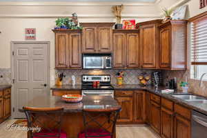 Kitchen featuring stainless steel appliances, tasteful backsplash, dark stone counters, and brown cabinets
