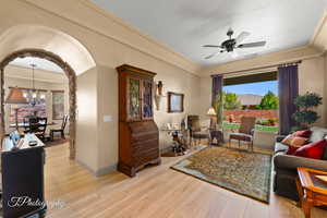 Living area with ornamental molding, light wood-type flooring, arched walkways, a ceiling fan, and a chandelier