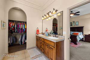 Ensuite bathroom with a walk in closet, light carpet, double vanity, light tile patterned flooring, and ceiling fan