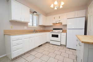 Kitchen with white appliances, butcher block countertops, white cabinetry, under cabinet range hood, and light tile patterned floors