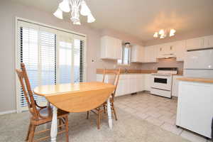 Kitchen with a chandelier, white appliances, white cabinets, and pendant lighting