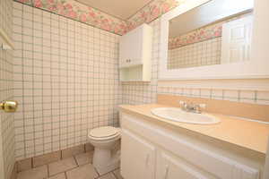 Bathroom with light tile patterned floors, vanity, wallpapered walls, and radiator heating unit