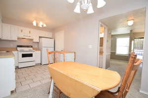 Kitchen with a chandelier, light colored carpet, white cabinetry, white appliances, and light countertops