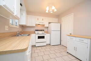 Kitchen featuring white appliances, white cabinets, under cabinet range hood, and a chandelier