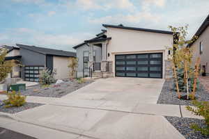 Modern home featuring concrete driveway, an attached garage, stone siding, and stucco siding