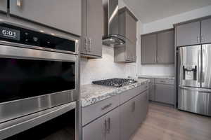 Kitchen featuring appliances with stainless steel finishes, backsplash, wall chimney exhaust hood, light wood-style flooring, and gray cabinets