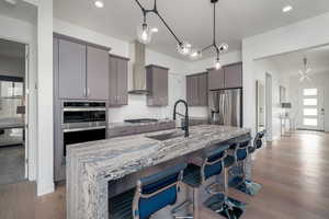 Kitchen featuring gray cabinets, decorative light fixtures, light wood-style flooring, an island with sink, and recessed lighting