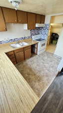 Kitchen with light countertops, brown cabinetry, white electric range oven, tasteful backsplash, and a textured ceiling