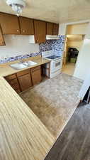 Kitchen featuring light countertops, brown cabinets, backsplash, electric stove, and a textured ceiling