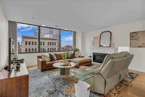 Living area with light wood-type flooring, a glass covered fireplace, a city view, and expansive windows