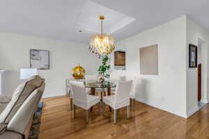 Dining room with light wood finished floors, a tray ceiling, and a chandelier