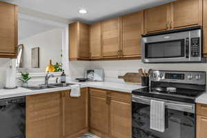 Kitchen featuring stainless steel appliances, light countertops, brown cabinets, and recessed lighting