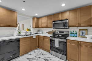 Kitchen featuring appliances with stainless steel finishes, light countertops, recessed lighting, light marble finish floors, and brown cabinets