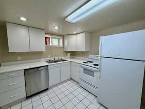 Kitchen featuring white appliances, light countertops, white cabinets, light tile patterned floors, and a textured ceiling
