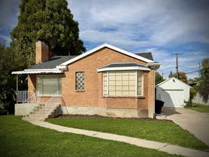 View of front facade with a front yard, an outbuilding, brick siding, and a detached garage