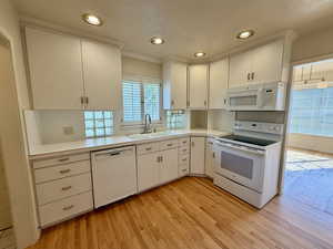 Kitchen featuring white appliances, light countertops, light wood-type flooring, recessed lighting, and white cabinets