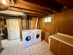 Laundry area featuring wooden walls, light tile patterned floors, and separate washer and dryer