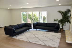 Living room with recessed lighting, wood finished floors, and a baseboard heating unit