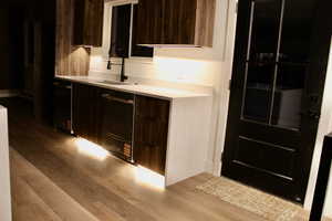 Bar area featuring modern cabinets, light wood-type flooring, dark brown cabinetry, light stone counters, and dishwashing machine