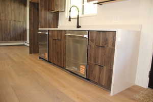 Kitchen featuring modern cabinets, light countertops, light wood-style floors, dishwasher, and dark brown cabinetry