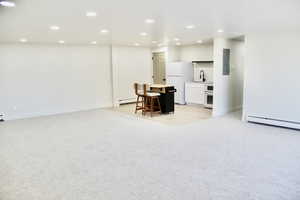 Basement featuring recessed lighting, light carpet, freestanding refrigerator, a baseboard radiator, and electric panel