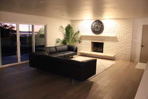 Living room featuring wood finished floors, a fireplace, and brick wall