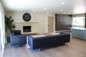 Living area with light wood finished floors, recessed lighting, baseboard heating, brick wall, and a fireplace
