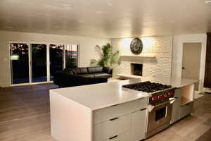 Kitchen with modern cabinets, premium stove, light wood-style floors, a brick fireplace, and open floor plan