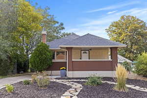 View of front of property with a shingled roof, a chimney, covered porch, and brick siding