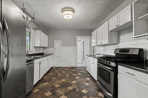 Kitchen with appliances with stainless steel finishes, white cabinetry, a wainscoted wall, a textured ceiling, and tile walls