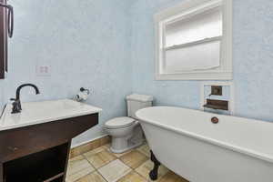 Full bathroom featuring vanity, a soaking tub, wallpapered walls, and light tile patterned floors