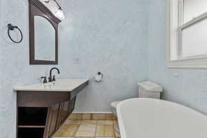 Full bathroom with vanity, a freestanding bath, light tile patterned floors, and a textured wall