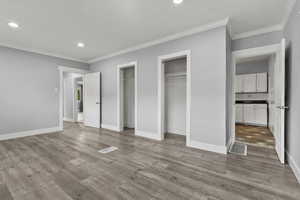 Unfurnished bedroom featuring two closets, ornamental molding, recessed lighting, and light wood-style flooring