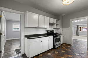 Kitchen featuring stainless steel range with gas stovetop, white cabinets, dark countertops, open shelves, and a textured ceiling