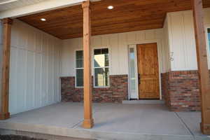 Property entrance with board and batten siding, a porch, and brick siding
