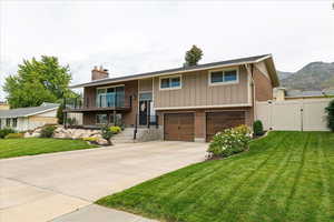 Split foyer home featuring brick siding, a balcony, a gate, driveway, and a chimney