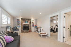 Living room featuring a stone fireplace, light carpet, built in shelves, and recessed lighting