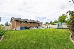 Back of property with a fenced backyard, a patio, brick siding, a playground, and a chimney