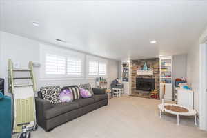 Living area featuring carpet, built in shelves, and a stone fireplace