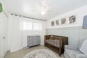 Carpeted bedroom featuring a decorative wall, a crib, ceiling fan, a wainscoted wall, and a closet