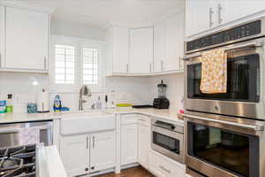 Kitchen featuring appliances with stainless steel finishes, white cabinets, decorative backsplash, and light stone counters