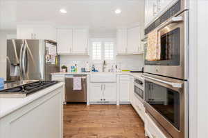 Kitchen with stainless steel appliances, white cabinetry, light wood-style flooring, decorative backsplash, and recessed lighting
