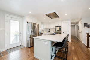 Kitchen with appliances with stainless steel finishes, dark wood finished floors, white cabinets, a center island, and recessed lighting